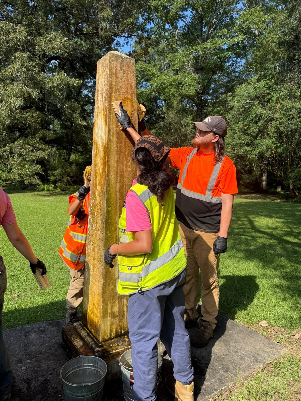 Participants carefully clean a historic cemetery monument under supervision
