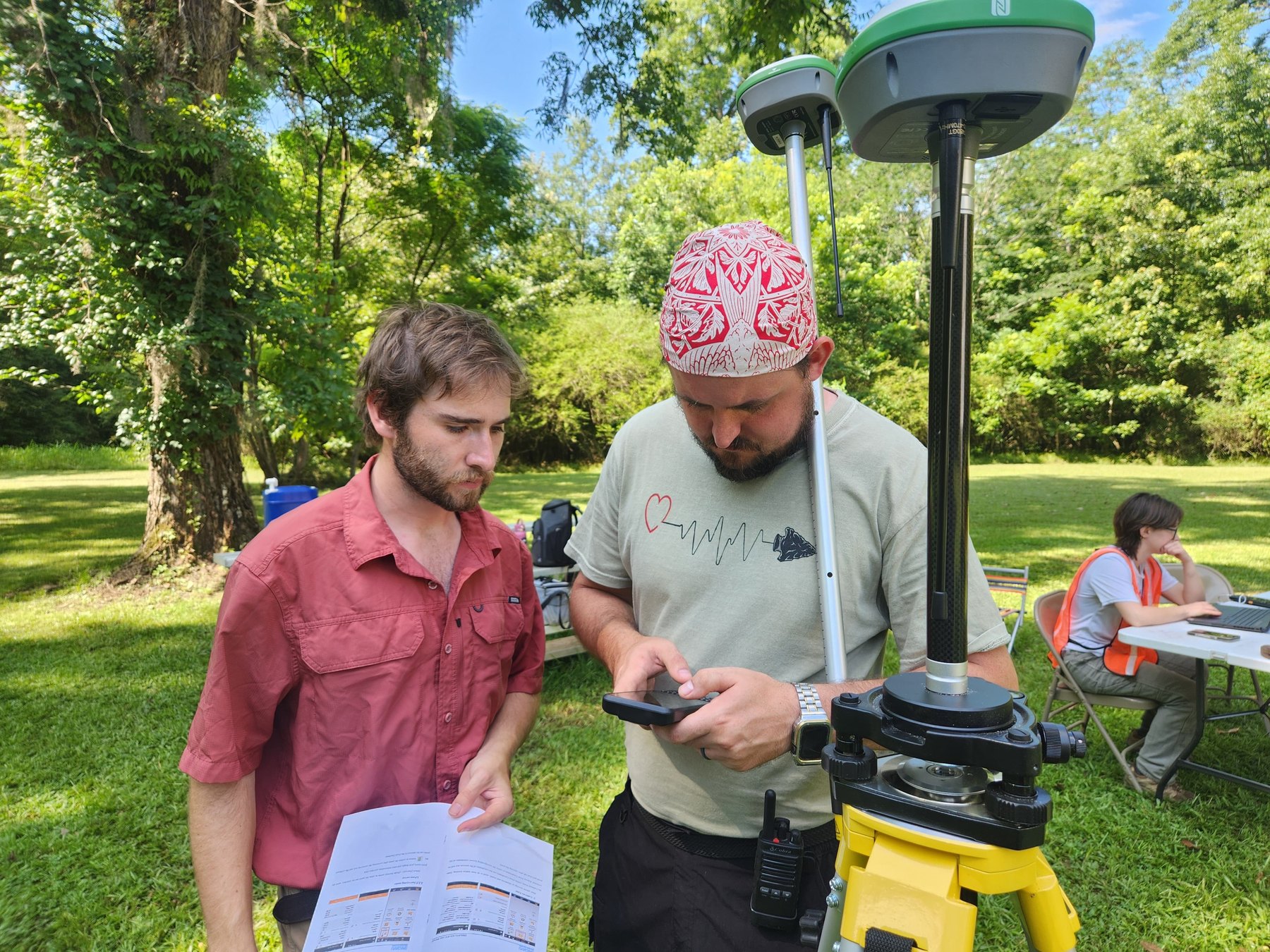 Instructor and participant review GNSS survey data beside a base and rover setup at Old Cahawba